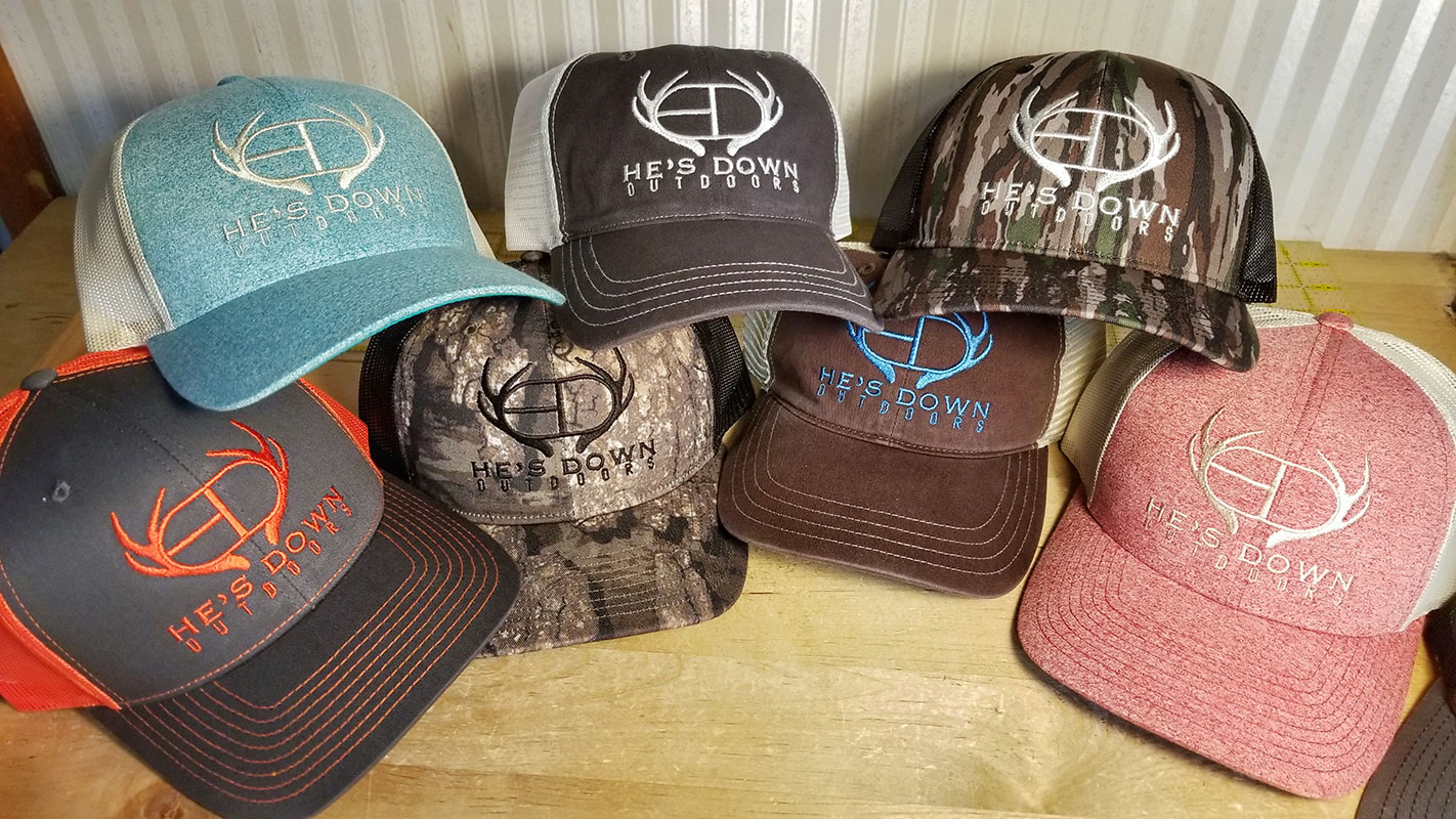 Seven baseball caps each embroidered with the He's Down Outdoors logo