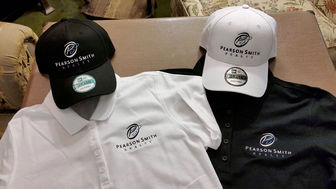 Two polo shirts and two baseball caps each embroidered with the Pearson Smith Realty logo