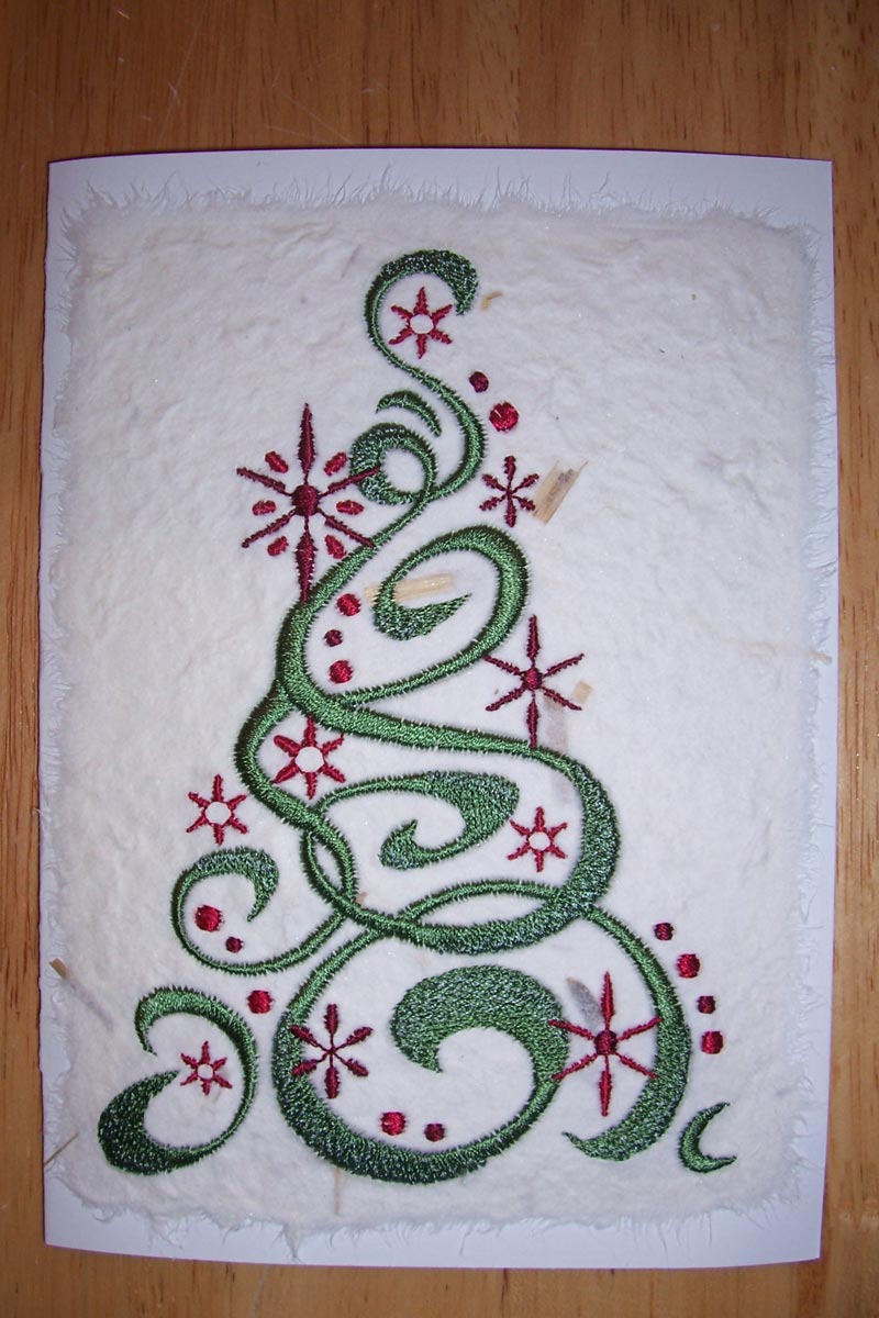 Christmas card, the front of which is an embroidered green stylized Christmas tree with red decorations on white textured paper.