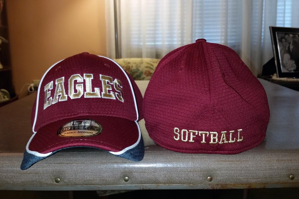 Maroon baseball caps, one facing front with the word EAGLES embroidered in gold, and one facing back with the word Softball embroidered in gold along the bottom edge of the cap.