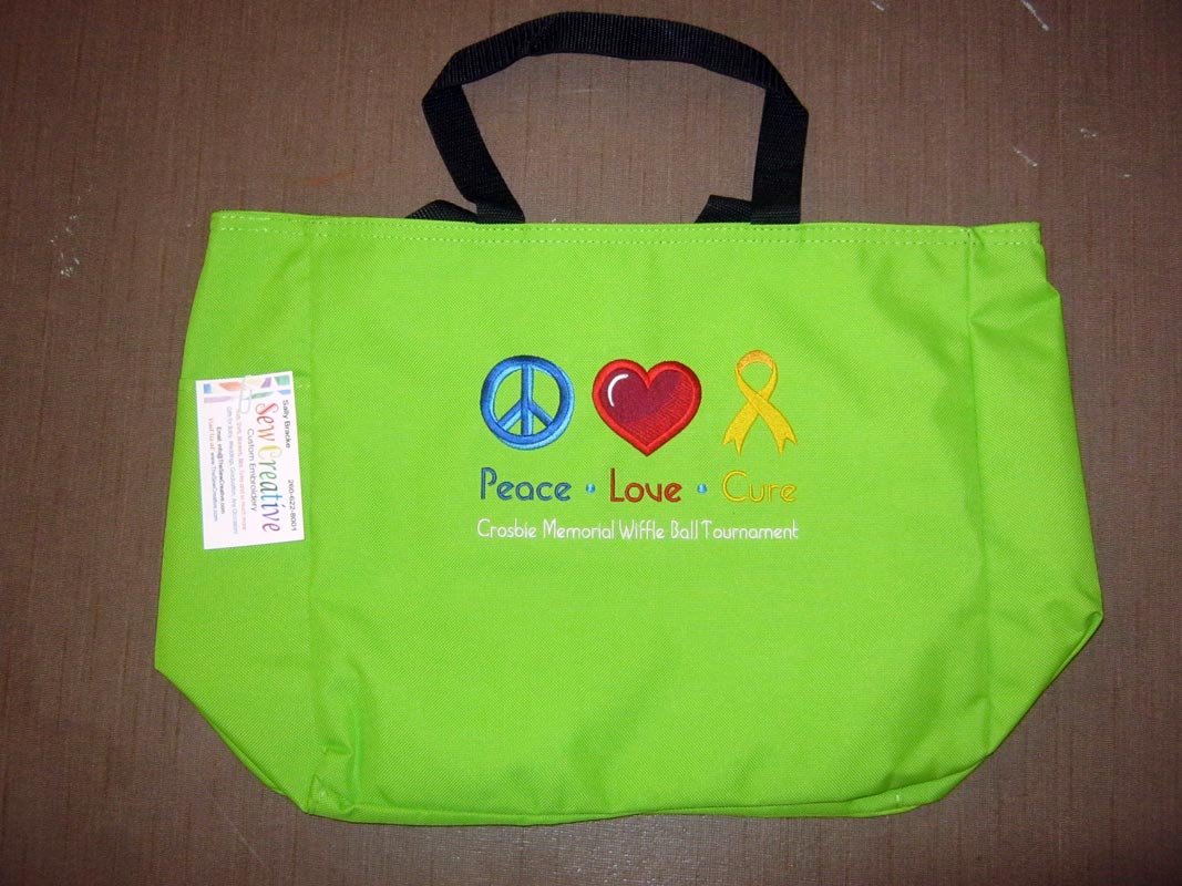 Bright green tote bag with black handles embroidered with a blue peace sign, red heart, and yellow cause ribbon. Below that in matching blue, red, and yellow text are the words Peace Love and Cure. Below that embroidered in white is the text Crosbie Memorial Wiffle Ball Tournament.