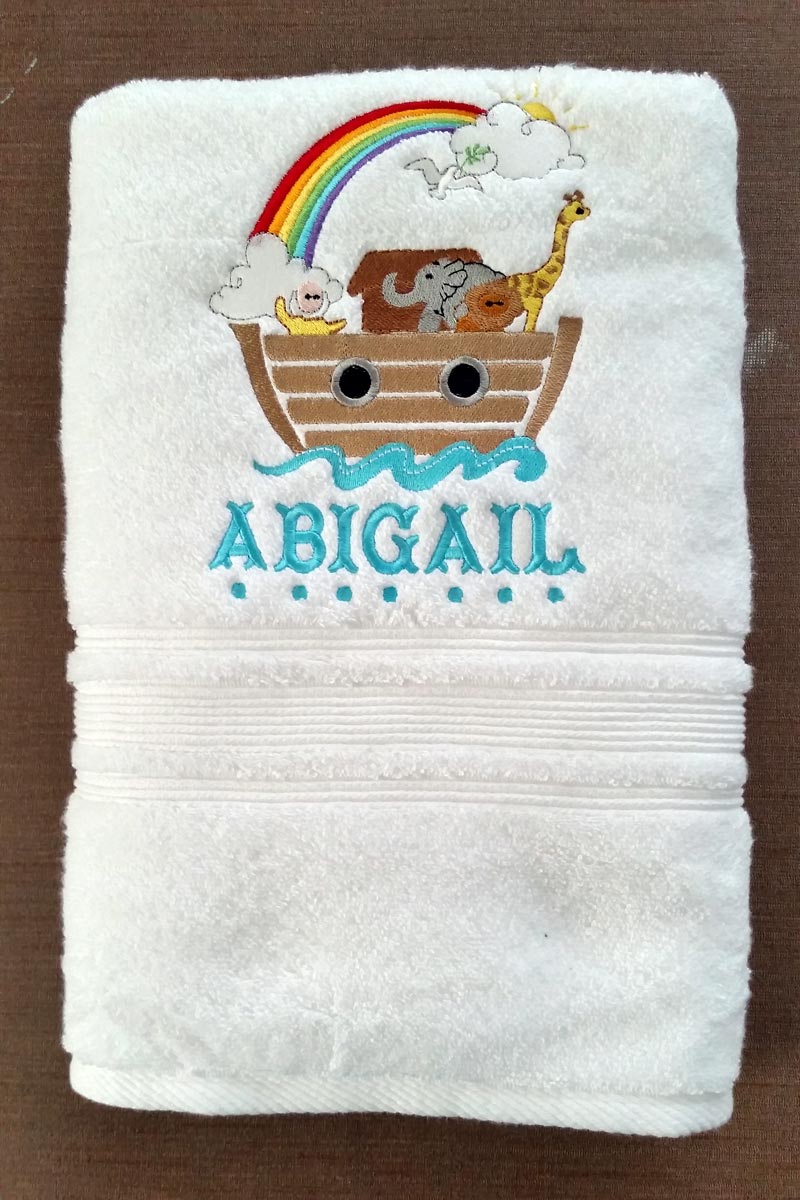 Child's bath towel with an embroidered design of Noah's Ark under a rainbow and the name Abigail underneath.