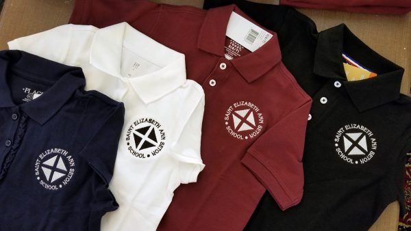 Four polo shirts in navy, white, burgundy, and black, each with the school logo embroidered on the left chest.