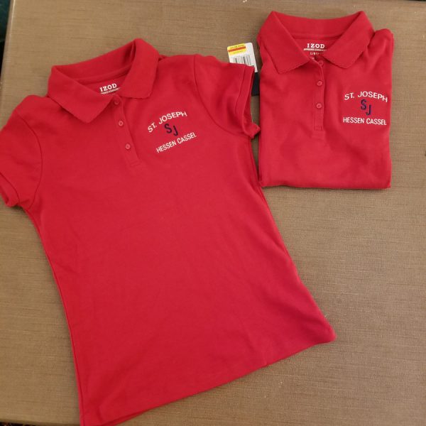 Two red polo shirts, one laid flat and one folded, each with the school initials and name embroidered on the left chest.